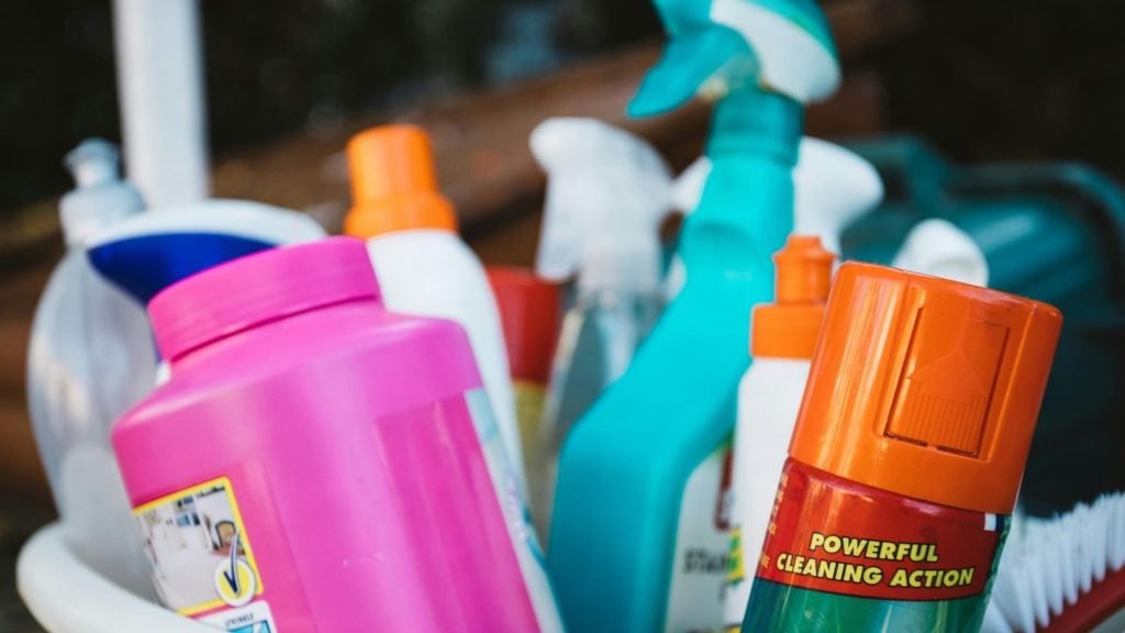 Close-up of colorful household cleaning bottles and spray cans in a bucket, one labeled “Powerful Cleaning Action