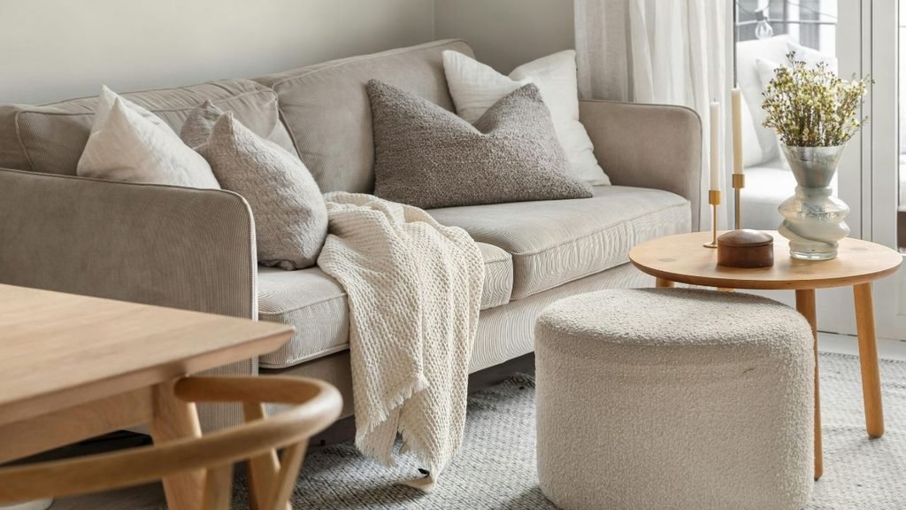 Cozy corner with a corduroy sofa, a bouclé ottoman and brass candlesticks on a round oak side table.