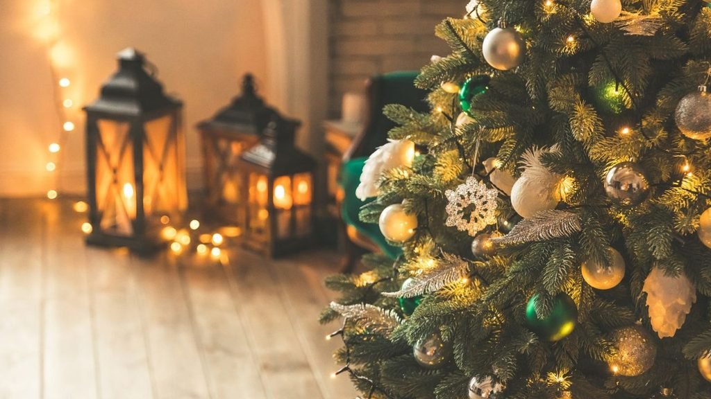 Close-up of a Christmas tree with silver, gold and green ornaments beside glowing lanterns, a cozy Christmas living room idea

