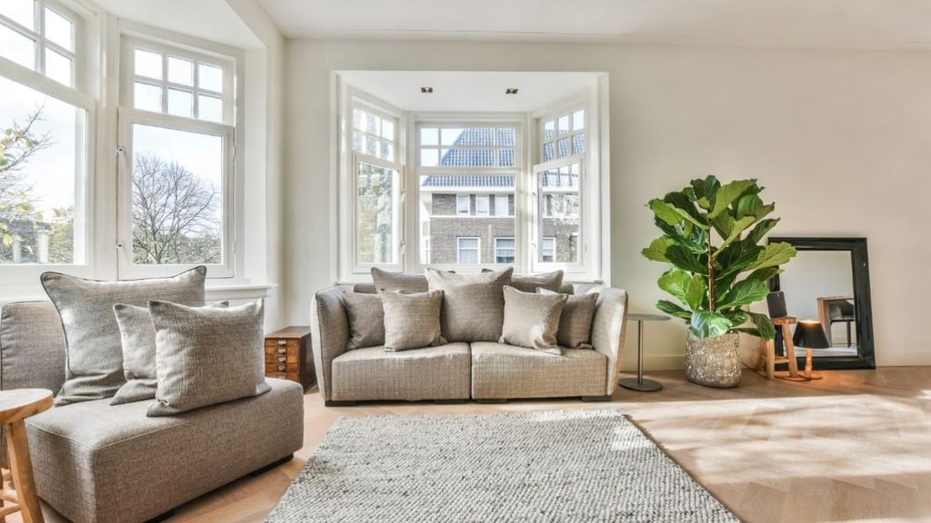 Gray sectional with patterned pillows, a corner fireplace and floral wall art in a bright living room.
