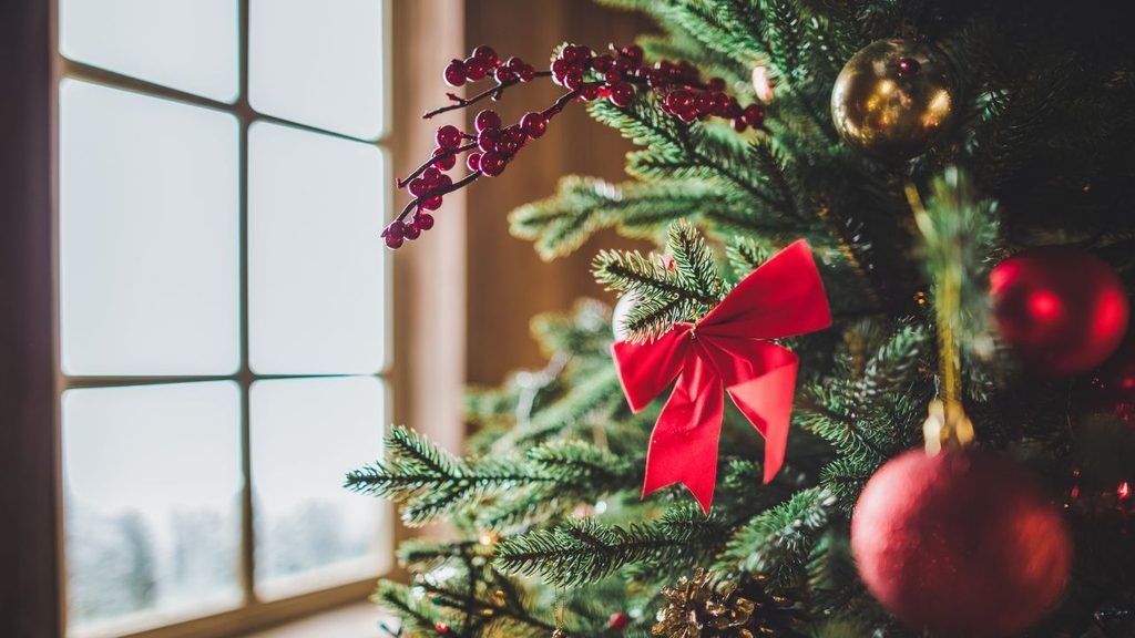 Eco-friendly christmas tree design idea using natural pine branches, red berries, a velvet bow and gold and red baubles by a window