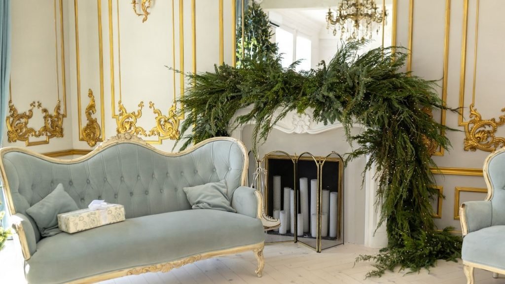 Festive living room Christmas decor with a lush evergreen garland on a white mantel above a powder-blue vintage sofa
