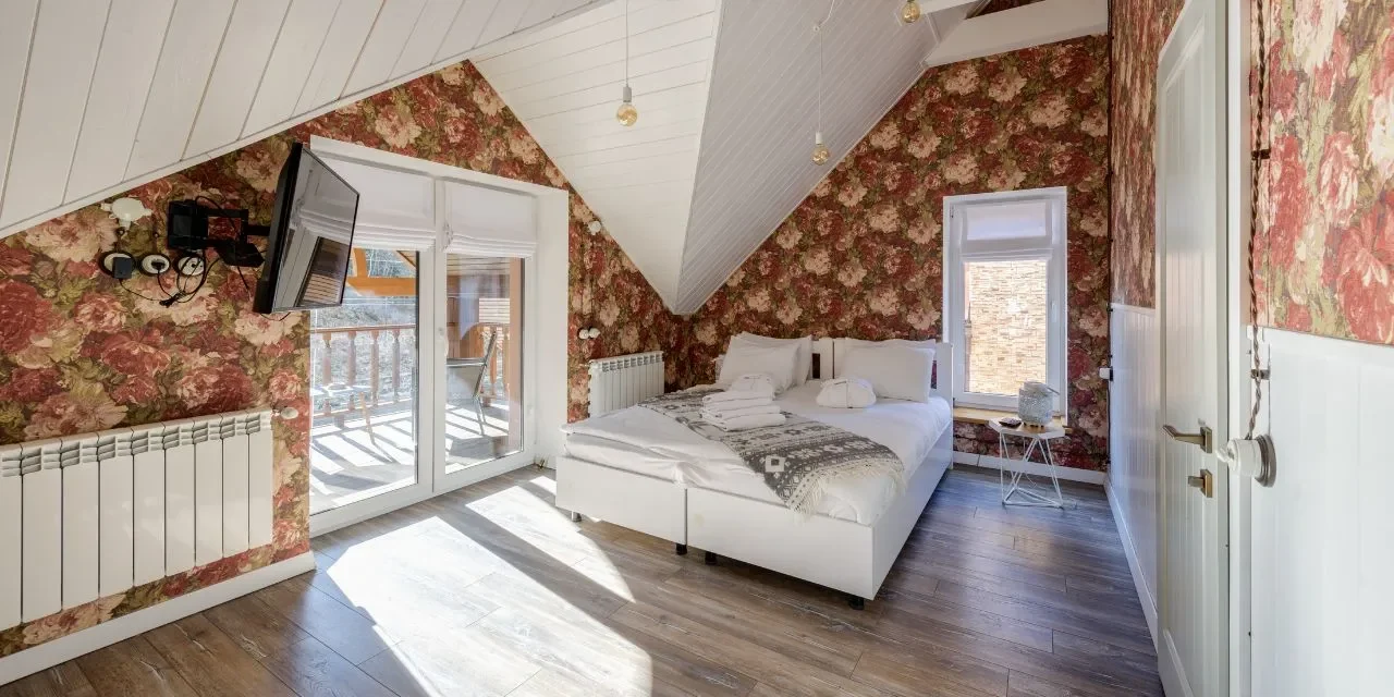 Cozy attic bedroom with vintage floral wallpaper for wall designs and bright natural lighting.