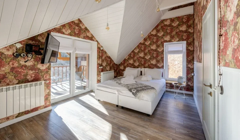 Cozy attic bedroom with vintage floral wallpaper for wall designs and bright natural lighting.