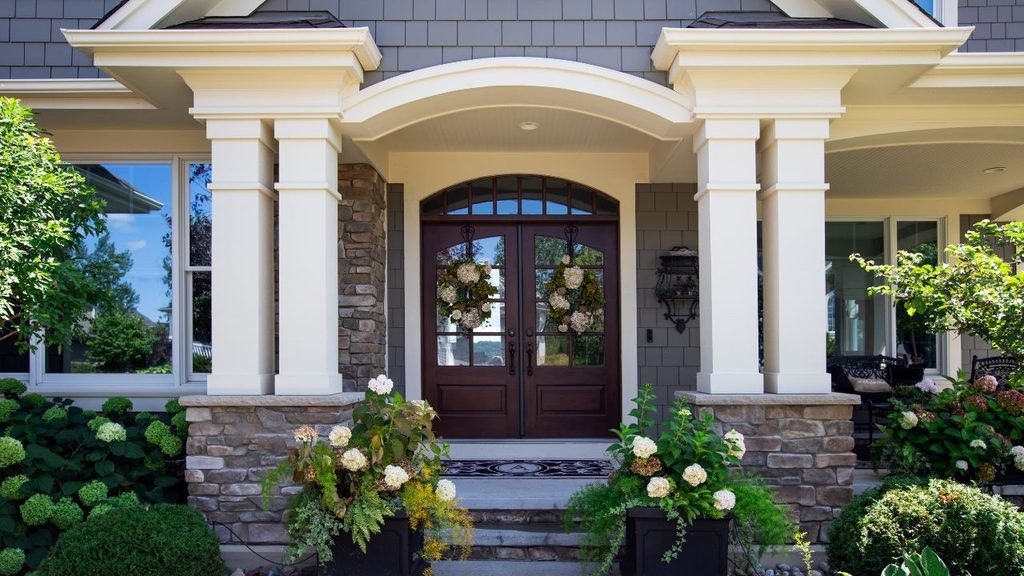 Front porch entrance with dark wood double doors, white square columns, stone bases and planters of white hydrangeas