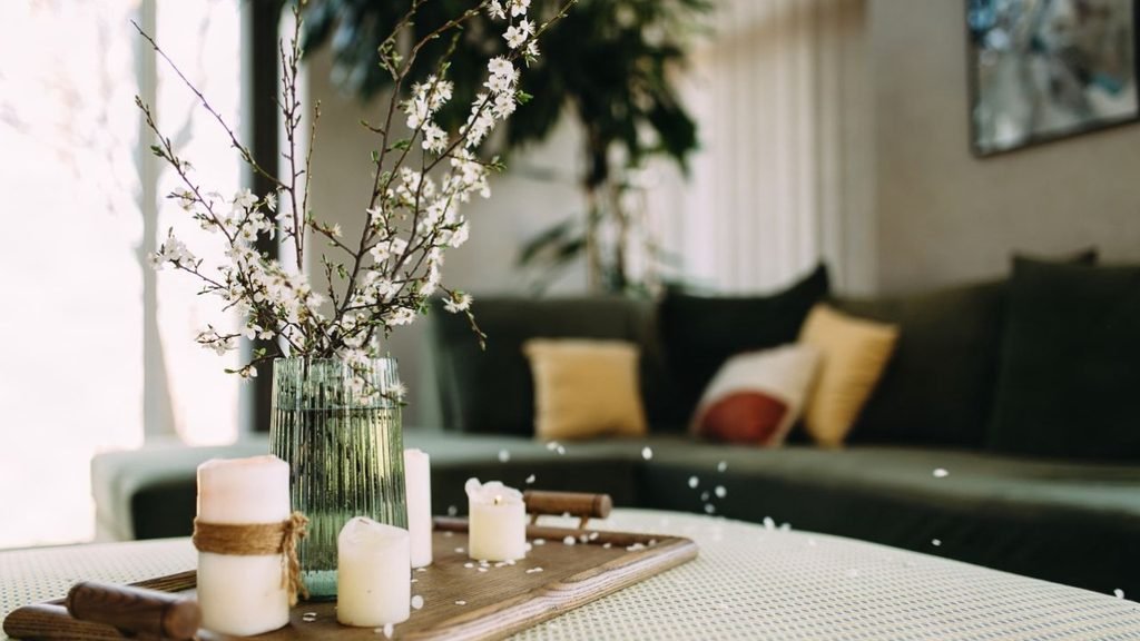 Holiday living room centerpiece idea with white pillar candles and blossom branches in a ribbed glass vase on a wooden tray