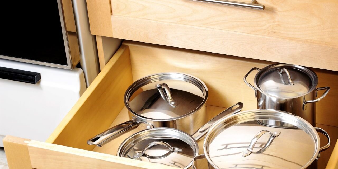 Kitchen drawer organization for deep drawers: stainless steel pots and saucepans with lids stored in a wooden kitchen cabinet drawer