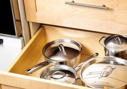 Kitchen drawer organization for deep drawers: stainless steel pots and saucepans with lids stored in a wooden kitchen cabinet drawer