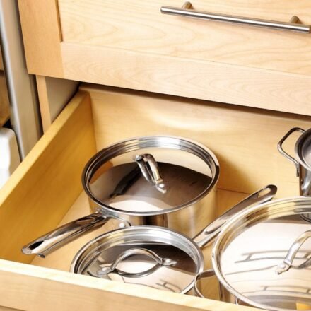 Kitchen drawer organization for deep drawers: stainless steel pots and saucepans with lids stored in a wooden kitchen cabinet drawer
