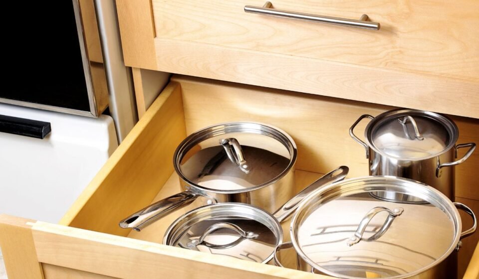 Kitchen drawer organization for deep drawers: stainless steel pots and saucepans with lids stored in a wooden kitchen cabinet drawer