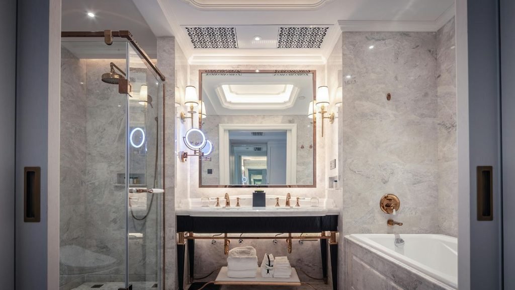 Luxury bathroom with gray marble walls, rose gold fixtures, double vanity, glass shower and built-in tub