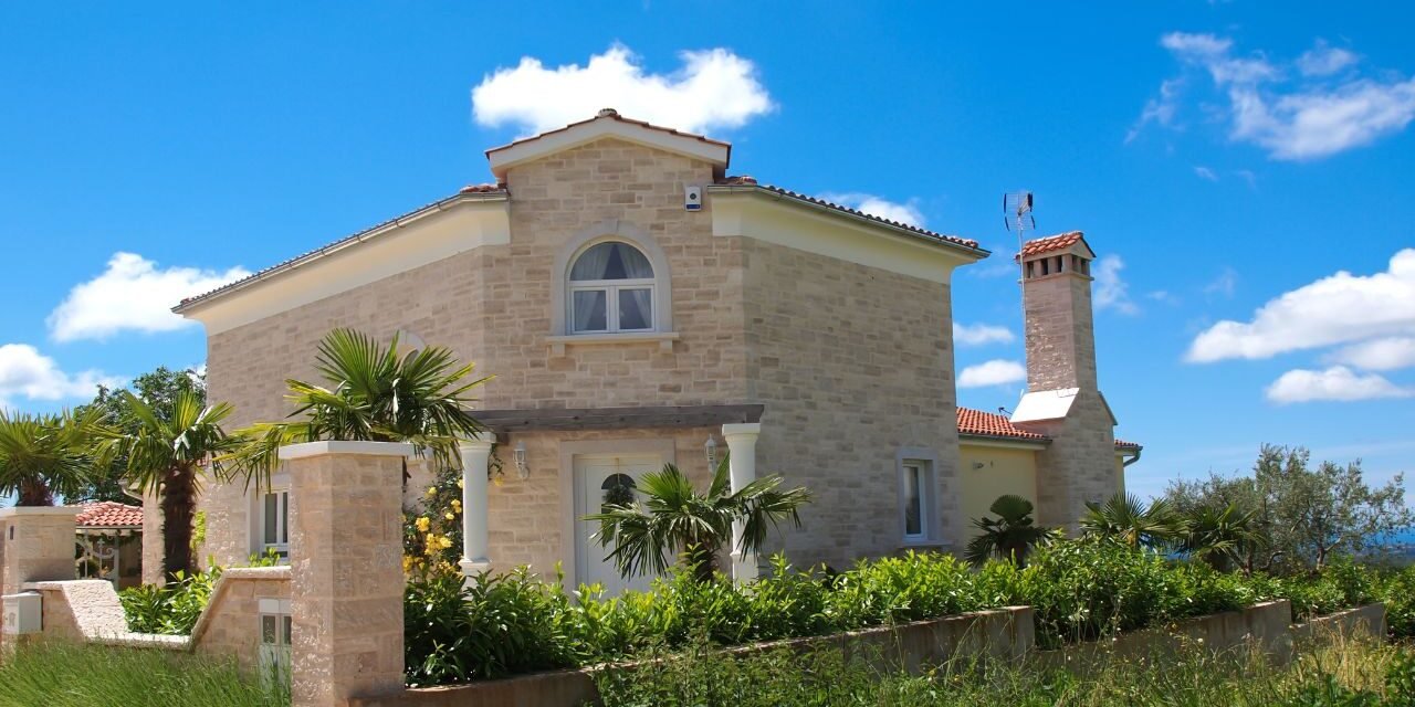 Mediterranean stone house in pale limestone with an arched window, terracotta roof tiles and palm trees