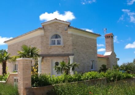 Mediterranean stone house in pale limestone with an arched window, terracotta roof tiles and palm trees