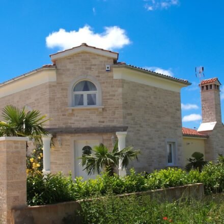Mediterranean stone house in pale limestone with an arched window, terracotta roof tiles and palm trees