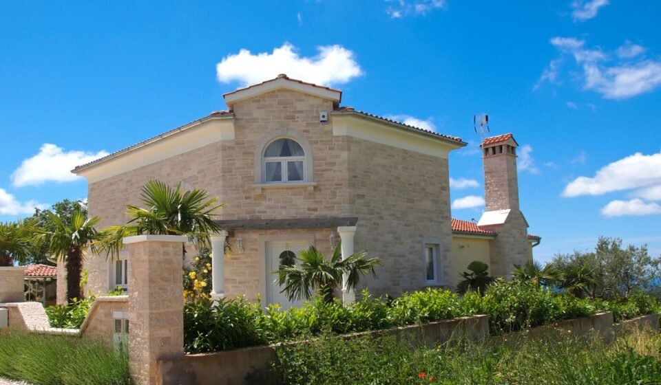 Mediterranean stone house in pale limestone with an arched window, terracotta roof tiles and palm trees