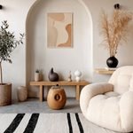 Minimalist cosy interior living room with a cream boucle armchair, arched wall niche, olive tree and a striped natural rug