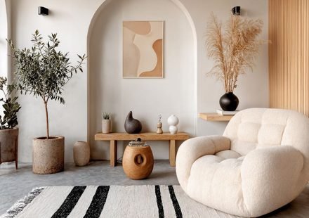 Minimalist cosy interior living room with a cream boucle armchair, arched wall niche, olive tree and a striped natural rug