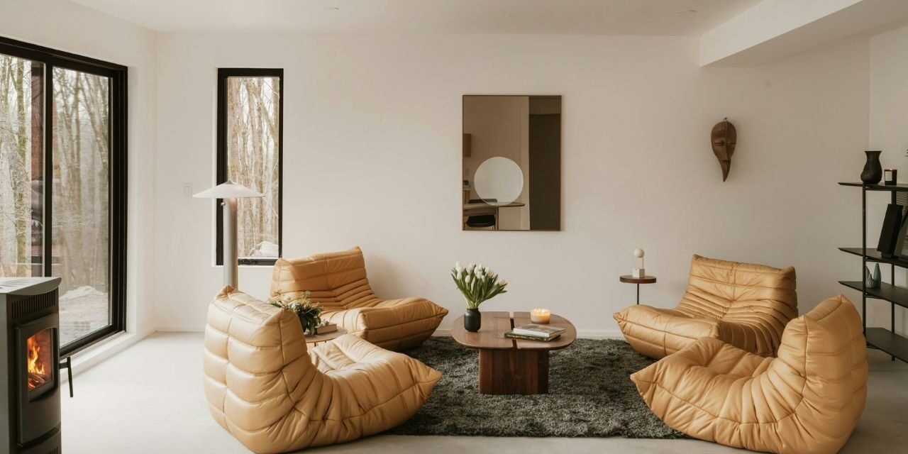 Minimalist cosy interior living room with a beige sectional sofa, floor-to-ceiling windows, built-in bookshelves and green plants