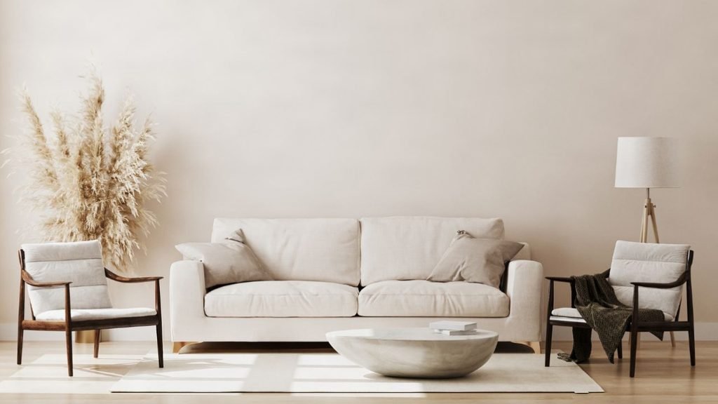 Modern neutral living room with a cream sofa, two wooden armchairs, pampas grass and a stone coffee table.