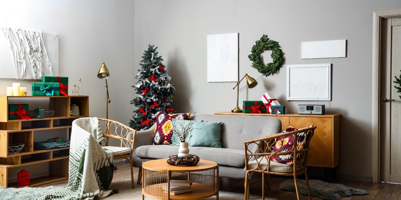 Neutral living room with rattan chairs, brass lamps, green wrapped gifts and a slim tree with red ribbons and silver bows