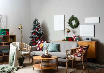 Neutral living room with rattan chairs, brass lamps, green wrapped gifts and a slim tree with red ribbons and silver bows