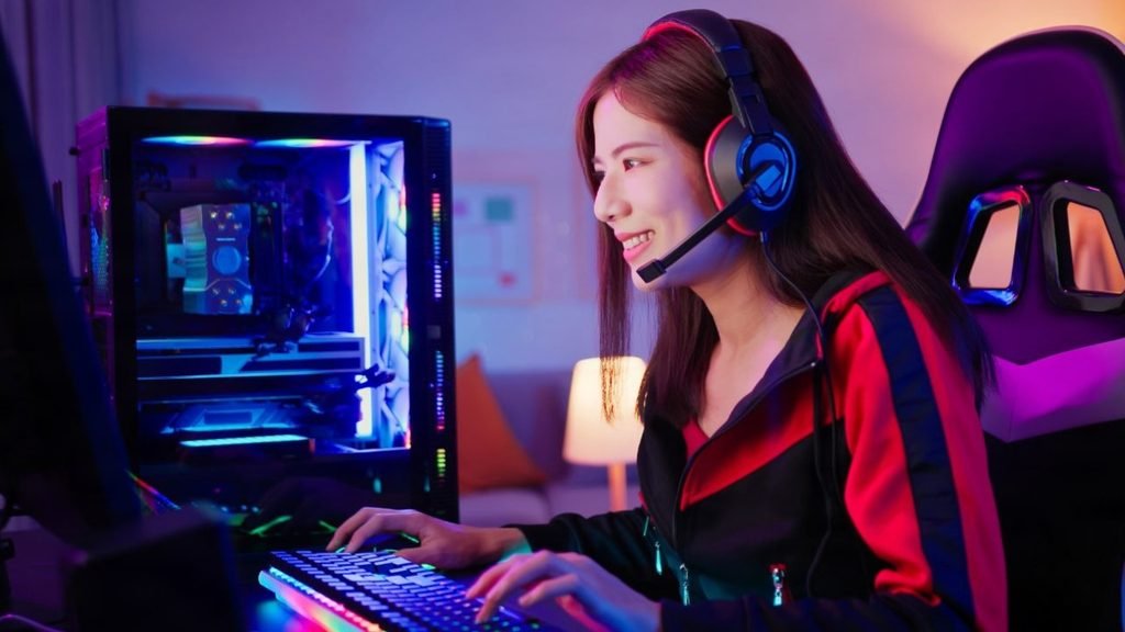 Girl playing on a pc gaming setup for a small room with an LED-lit PC case, gaming chair and warm lamp lighting