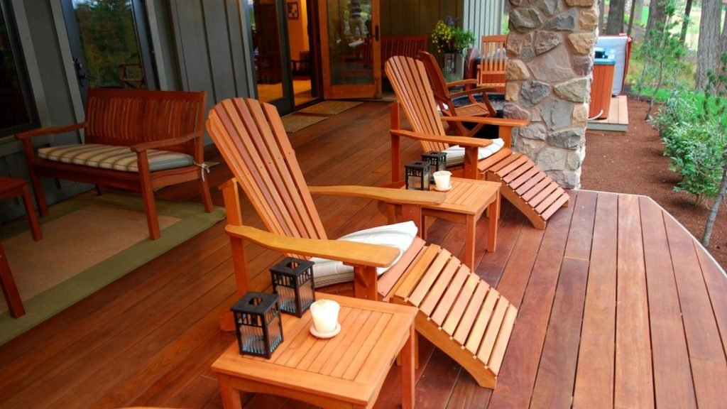 Polished hardwood porch deck with Adirondack chairs, footrests and lantern side tables, a relaxing setup among porch ideas for houses with a deck
