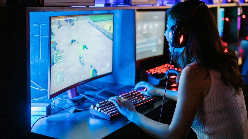 Woman gaming on a curved monitor with a backlit mechanical keyboard, a compact small room gaming setup that also suits a PS4