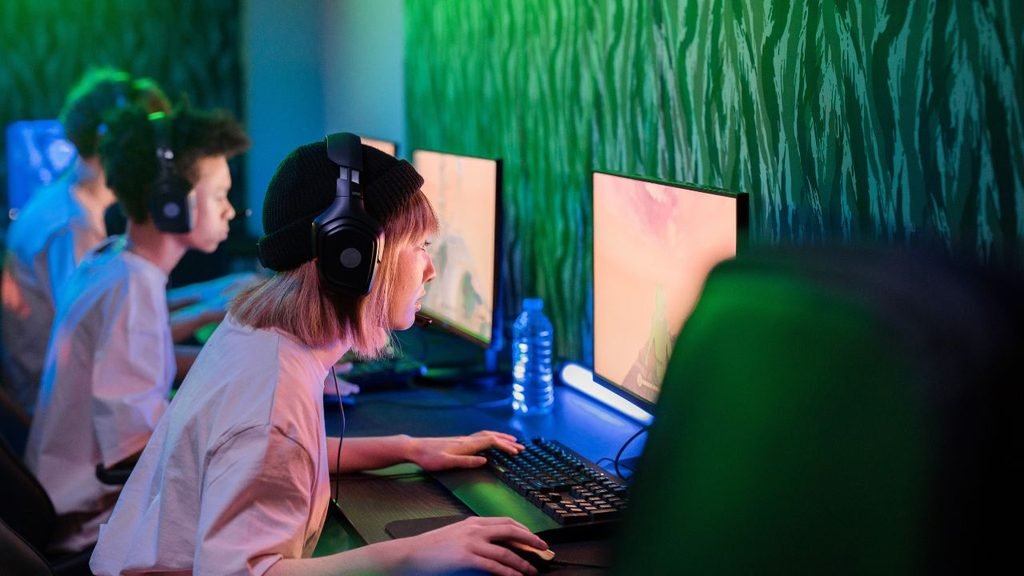 Gamers sitting in a row at a long desk with monitors and headsets, a layout often shared in small room gaming setup reddit threads