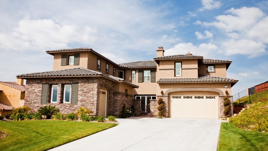 Stone house in modern style combining stone veneer and warm stucco with tile roofing, shutters and a wide driveway