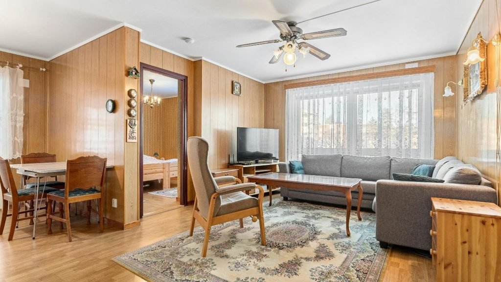 Warm living room with wood-paneled walls, a gray sectional, an armchair and a vintage oriental rug.