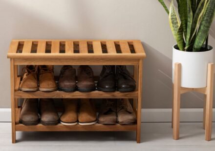 Wooden slatted shoe rack organizer bench with two shelves holding men's boots and leather shoes beside a potted snake plant